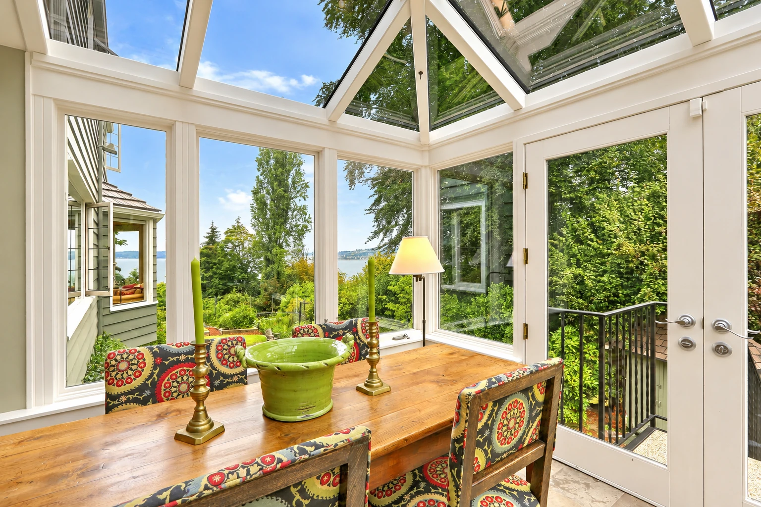 Bright solarium with a glass roof and white-framed windows, furnished with a wooden table and colorful chairs.