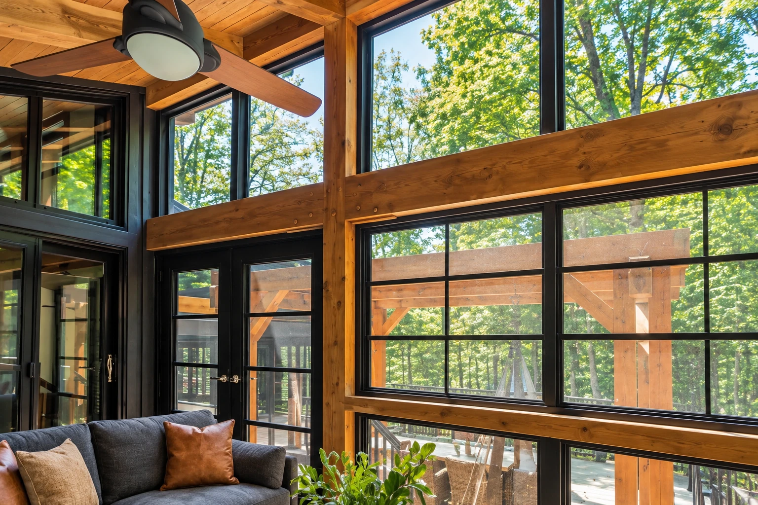 Sunroom with warm timber beams, large black-framed windows, a ceiling fan, and a sofa.